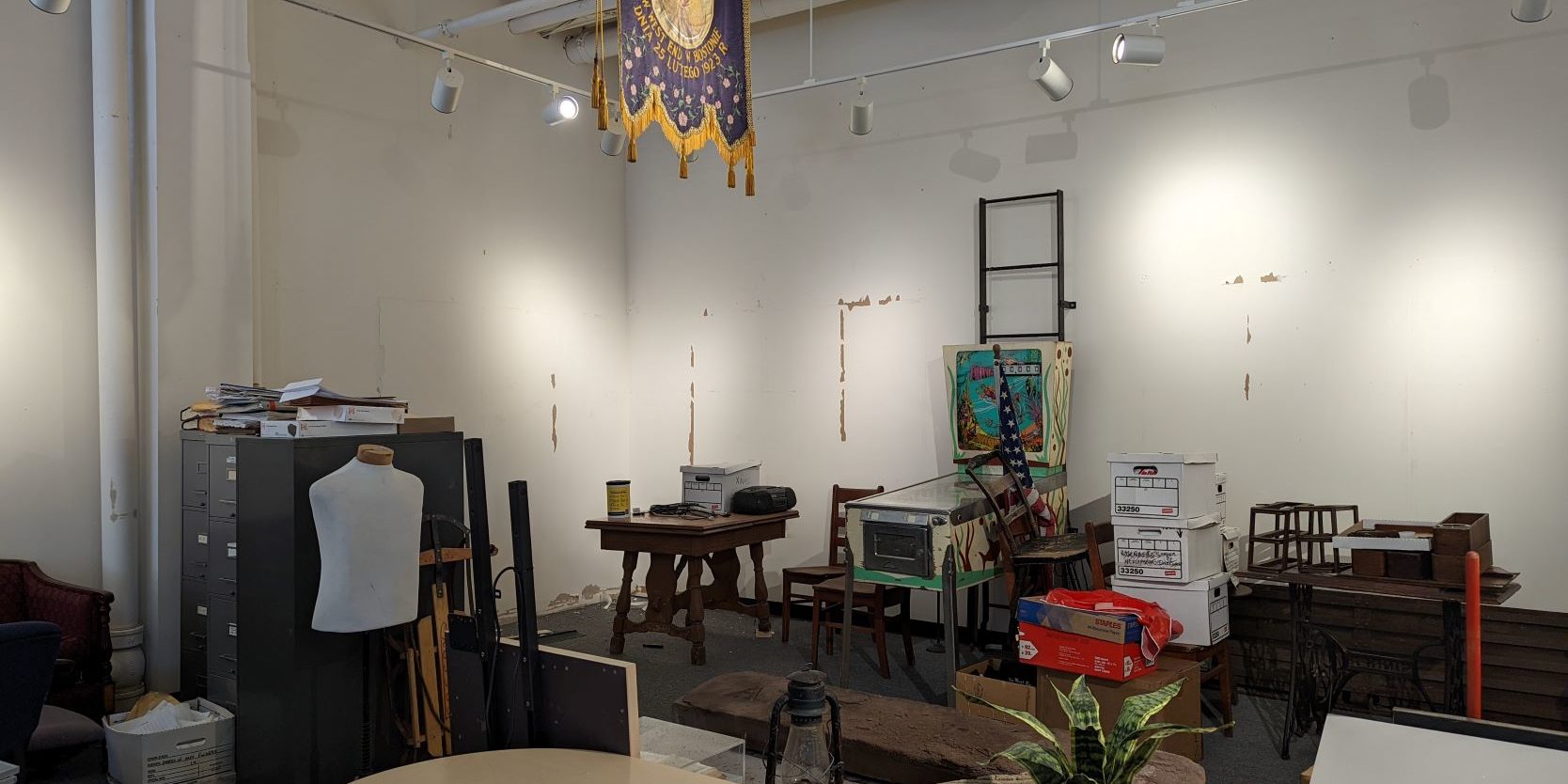 A room filled with a mess of file cabinets, tables, boxes, etc. The walls show marks where exhibits used to be