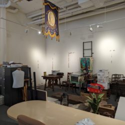 A room filled with a mess of file cabinets, tables, boxes, etc. The walls show marks where exhibits used to be