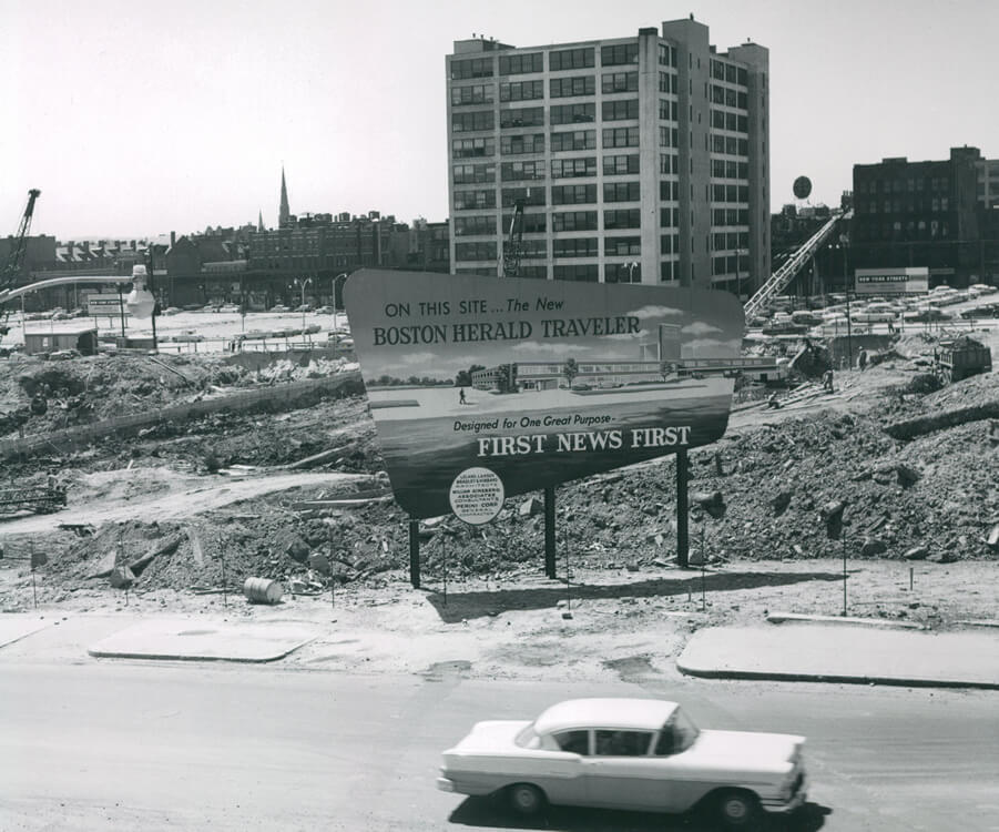 A demolished area with a sign marking the site of a new building for the Boston Herald Traveler