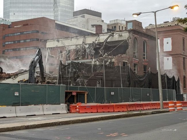 A historic building half collapsed with a crane knocking it down