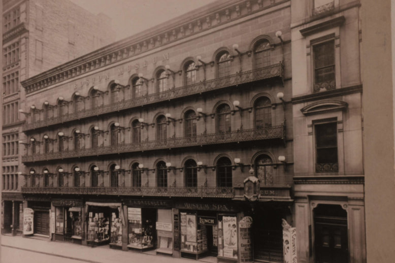 Photograph of a long four story stone building with store fronts on the street level