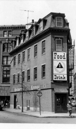 Photograph of a four story brick building at an intersection with a large sign over front door which says "Food" "Drink"