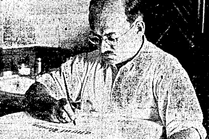 photograph of a man seated at a desk and working on a piece of calligraphy