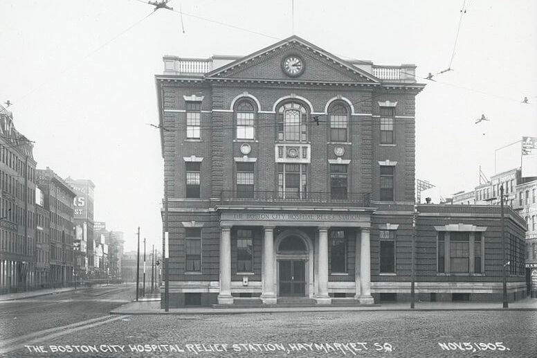 Photograph of the front of a three-story brick and masonry building, with two columns on either side of the front door.