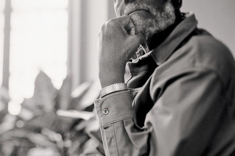 Photograph of a man posing in a charge with his hand to his chin