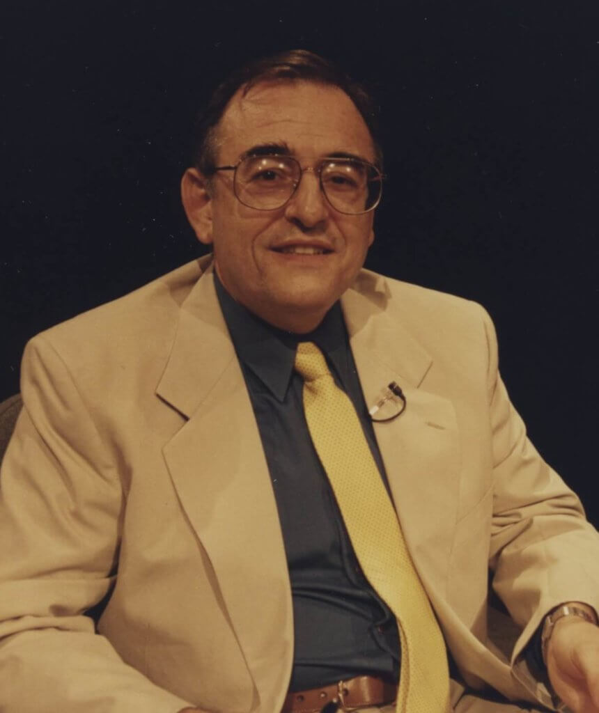 photograph of a man in a business suit posing for a photograph whole sitting in a chair.