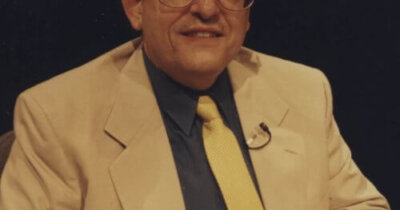 photograph of a man in a business suit posing for a photograph whole sitting in a chair.