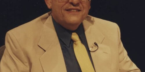 Campano 1990’s photograph of a man in a business suit posing for a photograph whole sitting in a chair.