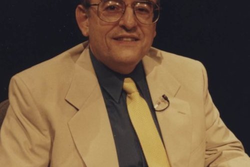 photograph of a man in a business suit posing for a photograph whole sitting in a chair.