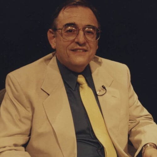 photograph of a man in a business suit posing for a photograph whole sitting in a chair.