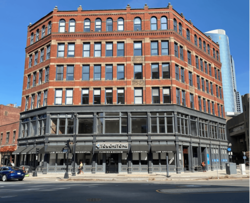 Photograph of the corner of a six-story brick and masonry building on a city street. The two bottom floors surrounding and above the main entrance is painted black. The sign over the door reads Touchstone. Pedestrians and carts are visible around the building.