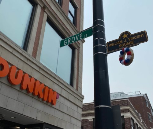 Photograph of a pole topped by a sign with a gold star and the words William J. Vincent. A wreath of flowers is placed below the sign.
