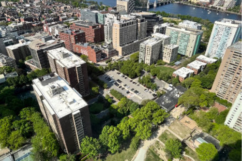 Aerial photograph of a city neighborhood featuring multi-story apartment buildings interspersed with trees and grassy spaces.