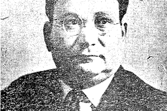Photograph of a man posing, wearing glasses and an suit and tie.