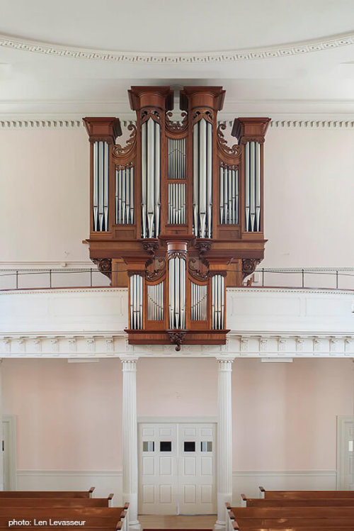 Photograph of a pipe organ located in the balcony of a church.