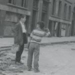 Two boys standing in a street by a demolished building