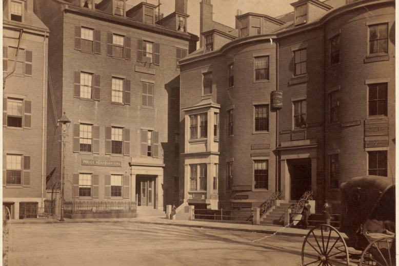 Photograph of a block of brick, bow-fronted, four-story buildings. The building in center has a sign that says Police Headquarters.