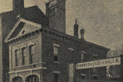 Photograph showing a two story brick building with two garage doors next to a sign stating "Sewer Dept. District 8".
