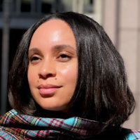 A woman of color with mid-length brown hair wearing a plaid scarf of red and teal