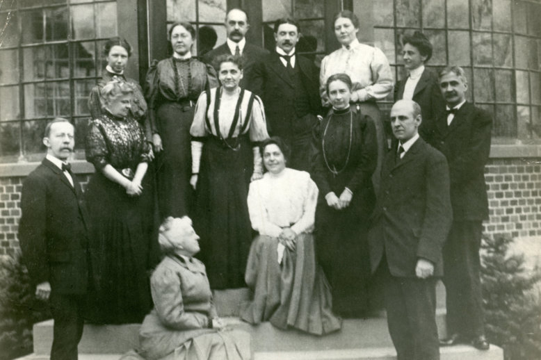 Photograph of a group of men and women posing on the steps of a brick and glass building.