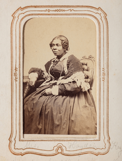Photograph of a Black woman seated, wearing a long dark dress.