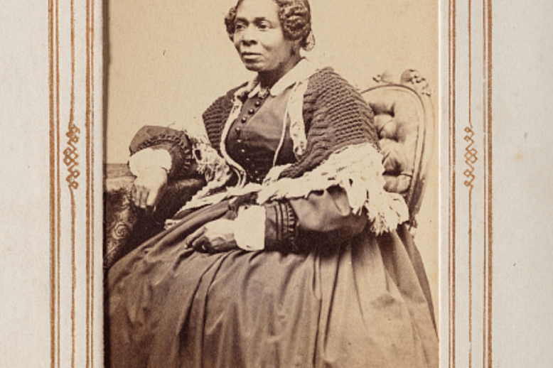 Photograph of a Black woman seated, wearing a long dark dress.