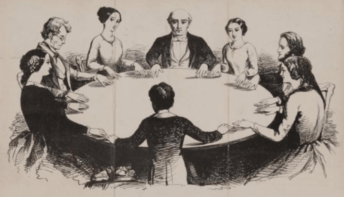 Men and women sit around a table for a seance.