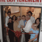 A group of people participate in a ribbon cutting, with a sign that says "The Last Tenement" above them.