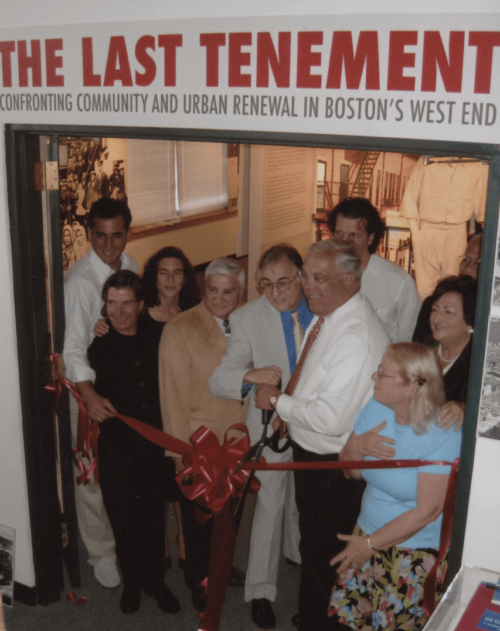 A group of people participate in a ribbon cutting, with a sign that says "The Last Tenement" above them.
