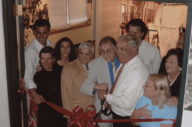 A group of people participate in a ribbon cutting, with a sign that says "The Last Tenement" above them.