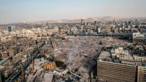 Photograph of demolished city blocks and a large clearing surrounded by intact and partially destroyed brick and masonry buildings.