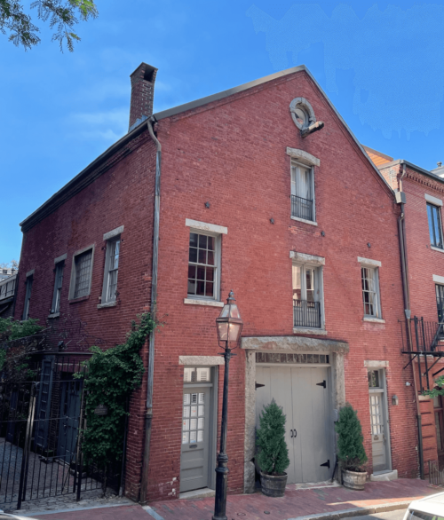 The brick façade of a building with a large wooden door and a triangle roof—distinctive from the typical roofs of the area.