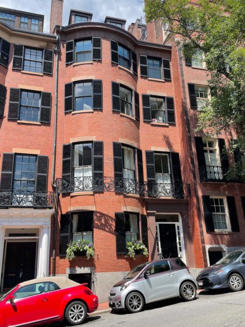 A color photograph of a four-story brick building (plus two windows to an attic) with rounded bay windows and black shutters.