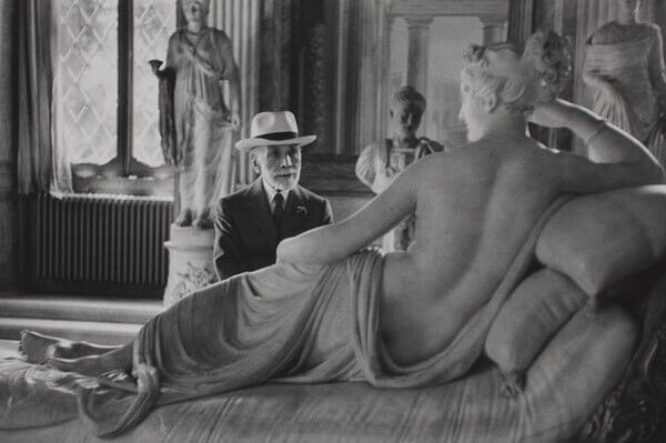 Bernard Berenson at 90 inside a museum gallery. He sits in front of a marble statue of a reclining nude.