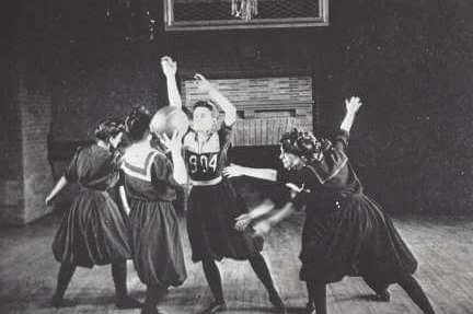 Four women play basketball in dresses.