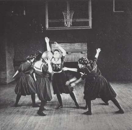 Four women play basketball in dresses.