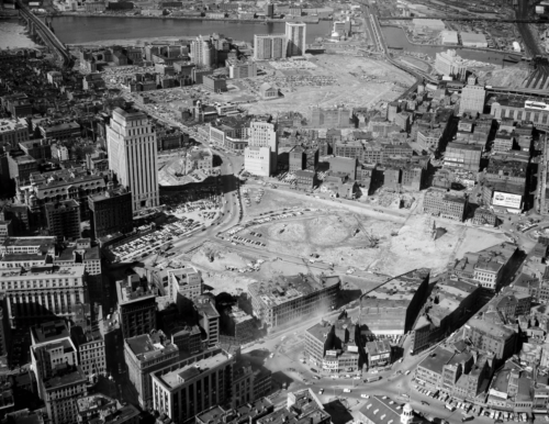 A black and white photographed of demolished land. The leveled area stands in contrast to the still-standing buildings that surround it.