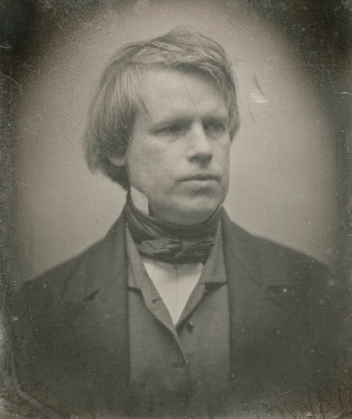 A black and white photograph of a clean-shaven man, wearing a two piece suit.
