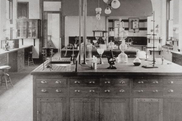 A black and white photograph of a nineteenth-century medical laboratory, showing microscopes, vials, and other medical instruments.