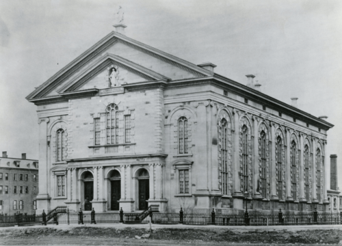 A black and white photograph of a grand church building, with classical arches, statues, and large stained-glass windows.