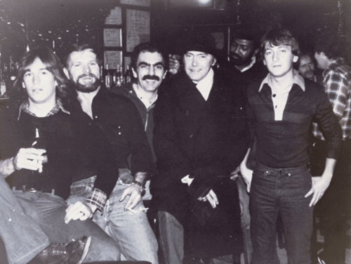 A black and white photograph of five men sitting inside a bar.