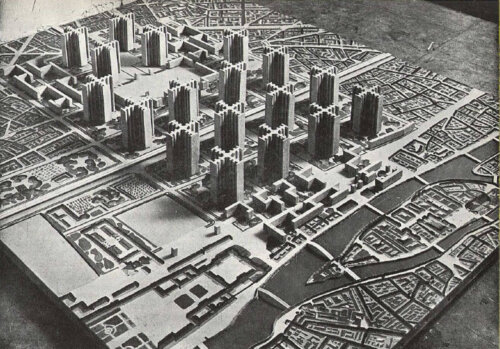 A black and white photograph of a model city, showing towers within park spaces next to a river.