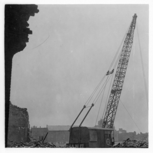 Black and white photograph of a torn down building and a crane.