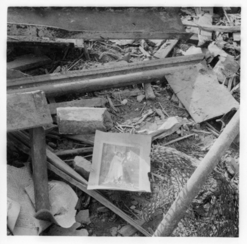 Black and white photograph of a wedding photograph laying in rubble.