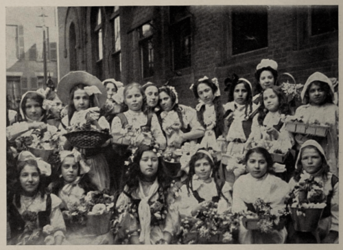 A black and white photograph of young girls standing outside holding flowers.