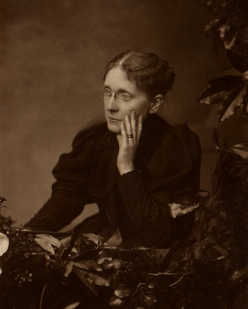 A sepia toned photograph of a woman in Victorian dress, her head rested in her hands.