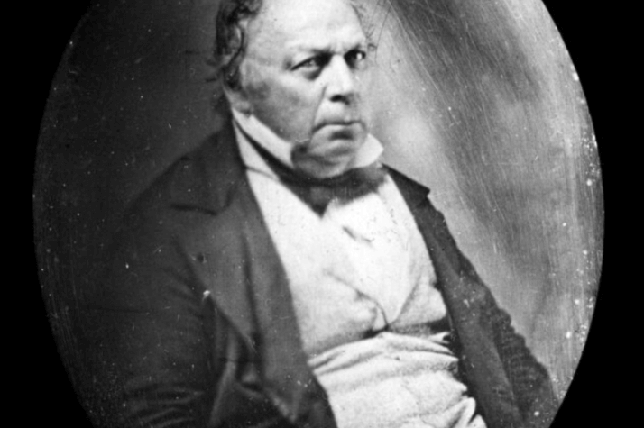 Alexander Parris A black and white photograph of an older man, seated and looking at the camera. He wears a suit.