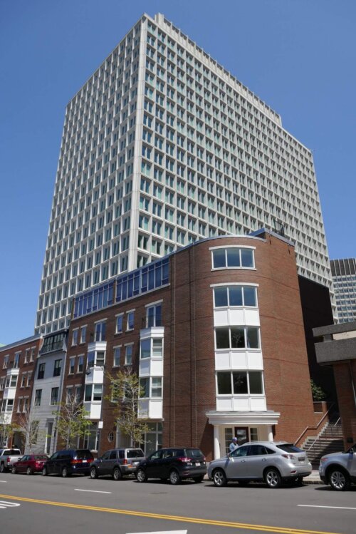 A photograph of a tall art deco building, fronted by smaller brick residential buildings on a city street.