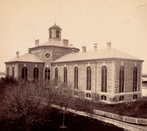 A black and white photograph of a large cruciform-layout granite building, with large windows and a rotunda.
