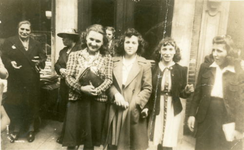 A black and white photograph of 7 women, wearing skirts and blazers, standing in front of a city building.